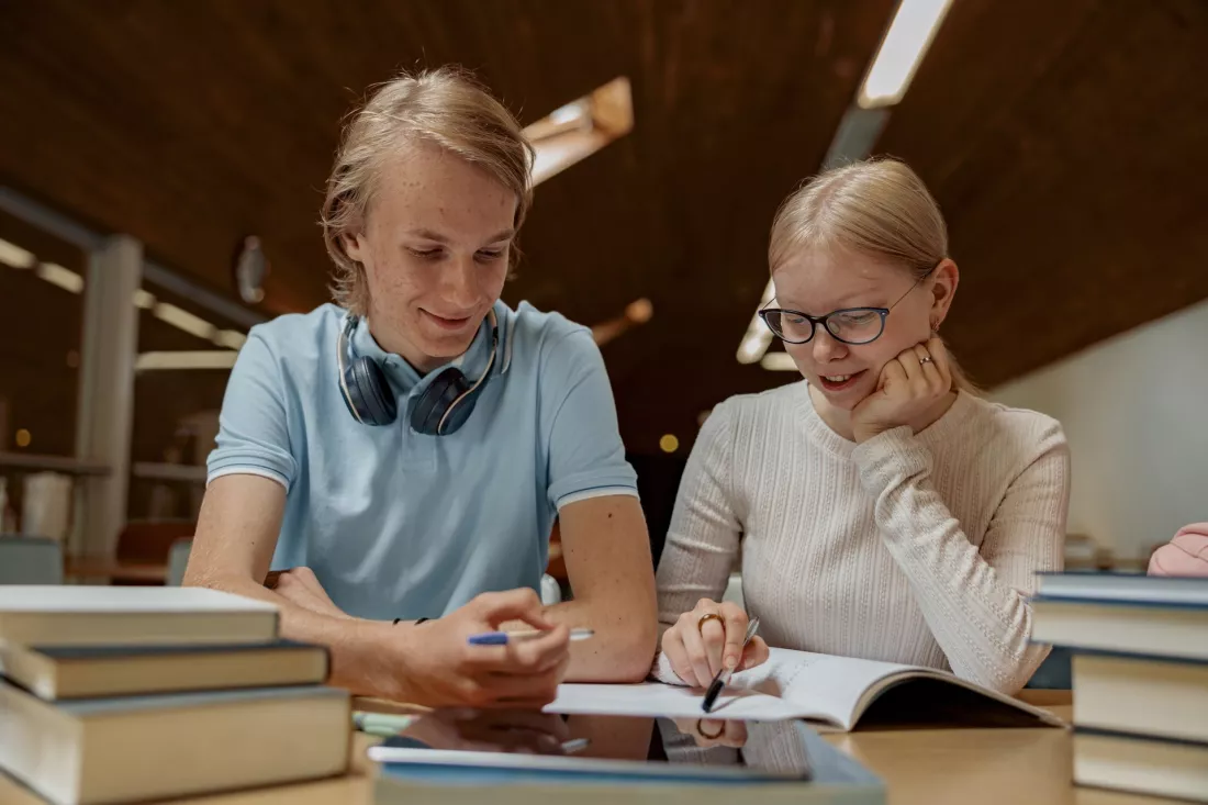 Dwoje studentów robi notatki przy stole w bibliotece