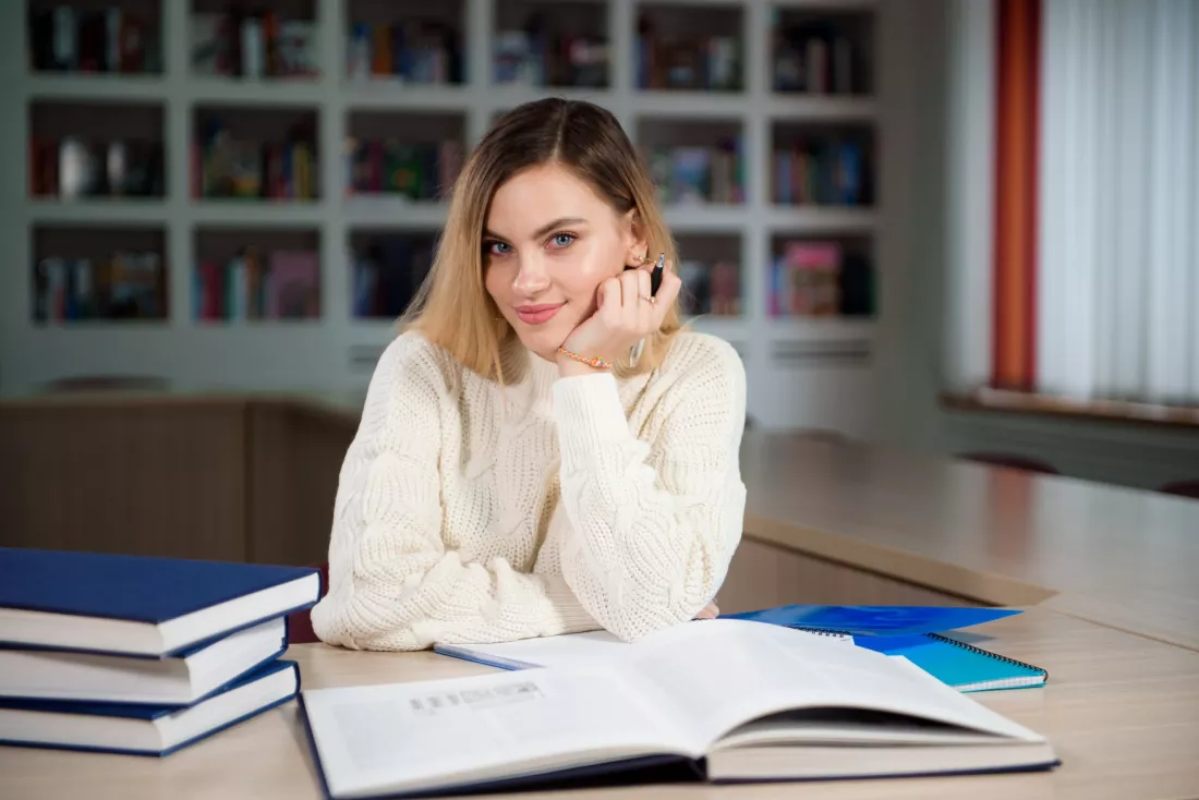 A young woman takes notes from a book in a library.
