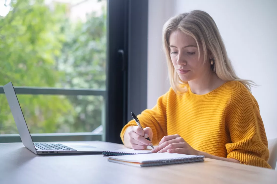 Studentka robi notatki przy laptopie w domu