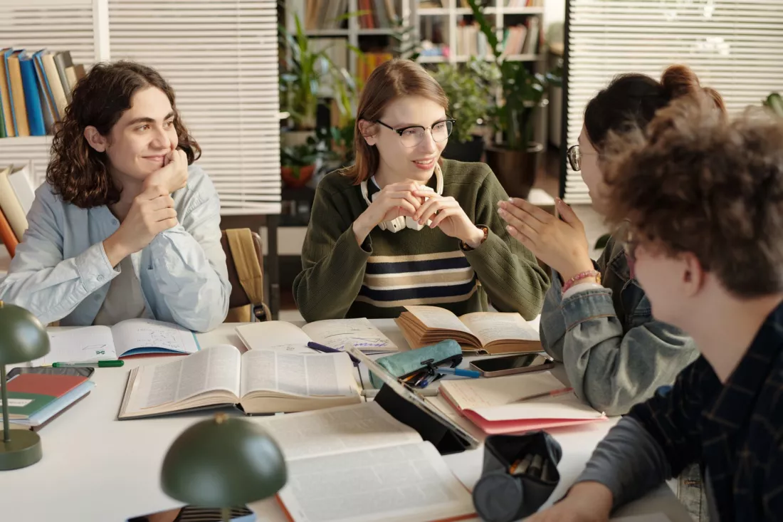 Studenci rozmawiaja przy stole podczas nauki jezyka w malej grupie