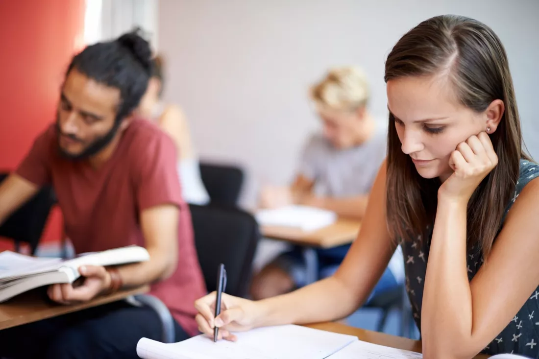 Studentka rozwiązuje pisemny test w sali, obok inni studenci