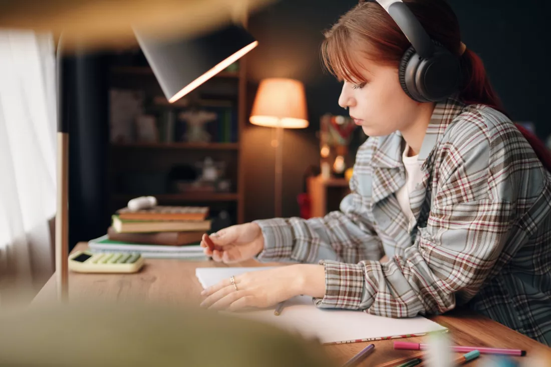 Teenage girl with headphones studying at a desk with notes