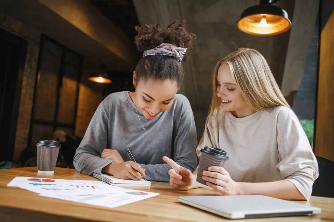 Dwie studentki uczą się razem z notatnikami przy stoliku w kawiarni