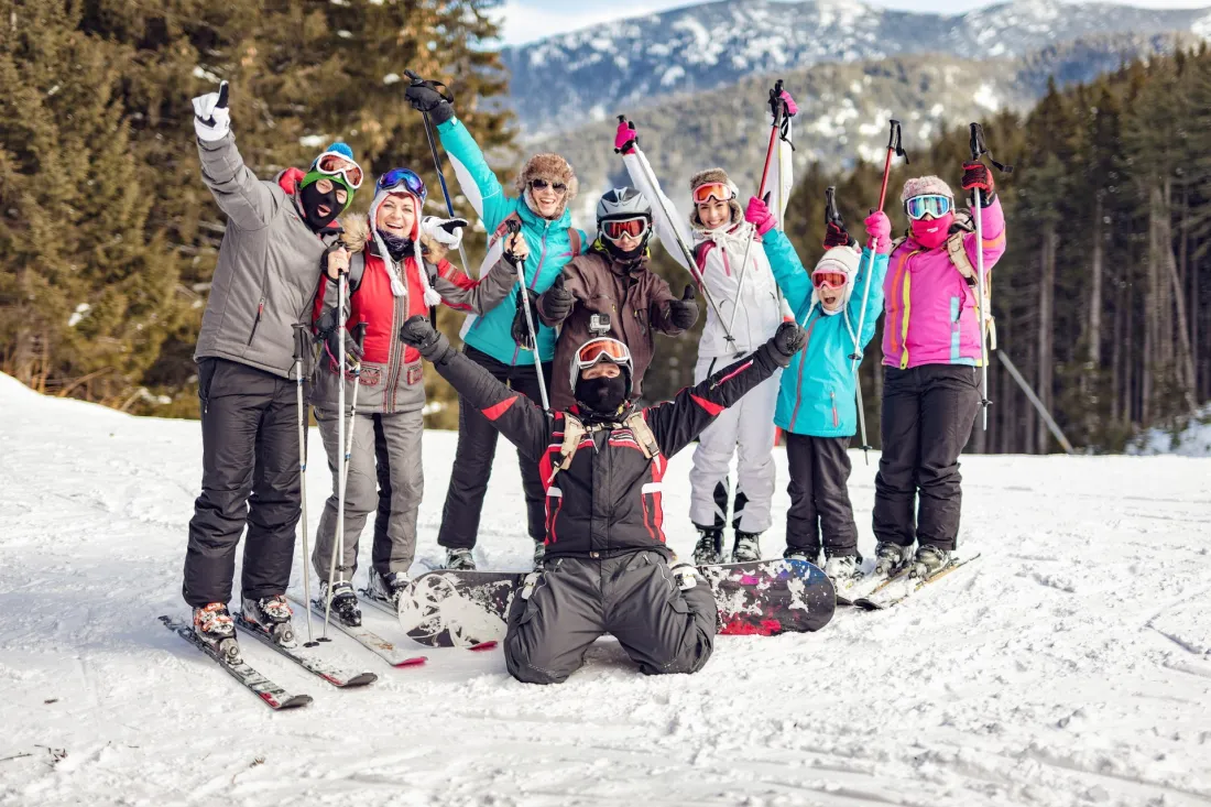 Grupa na nartach i snowboardach cieszy się na ośnieżonym stoku w górach